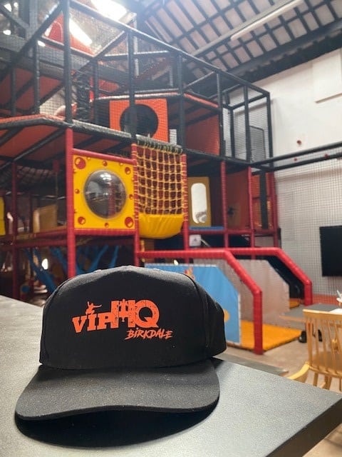 Image shows a cap with VIP HQ branding as well as the soft play centre in the background.